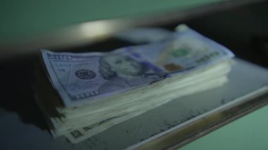 Yüzlerce dolarlık banknotların yakın plan görüntüsü loş bir ortamda düzgünce bir masanın üzerine istiflenmiş.