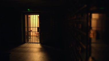 Uzakta loş ışıklı bir hücresi olan karanlık bir hapishane koridoru sinematik ve karamsar bir atmosfer yaratıyor.