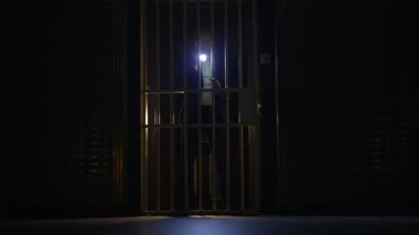 Loş bir ortamda parmaklıkların arkasında pusuya yatmış ürkütücü bir figür gizemli bir ortam yaratıyor.