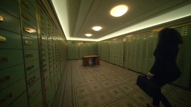 İçinde kiralık kasalar, ahşap masalar ve belgelerle ilgilenen bir kişi olan klasik bir banka kasasının iç görüntüsü..
