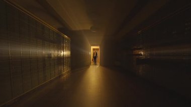Karanlık bir koridorda arka planda açık bir kapıdan gelen ışıkla yürüyen bir insan silueti..