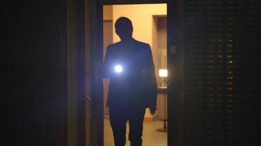 Bir güvenlik görevlisi, güvenlik önlemlerinin alındığından emin olmak için gece vakti el feneriyle tesisi teftiş ediyor.