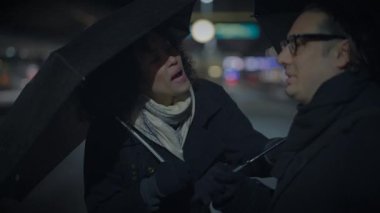 Gece yarısı karanlığında, bir adam ve bir kadın yağmurda şemsiyenin altında durup bir anlık fotoğraf çekiminde eğleniyorlar.