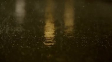 Gece ıslak bir yüzeye düşen yağmur damlalarının büyüleyici bir görüntüsü, ışıkları yansıtıyor, büyüleyici bir görsel yaratıyor.