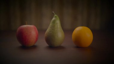 Bir elma, bir armut ve bir portakal da dahil olmak üzere çeşitli meyveler ahşap bir masaya konur ve renkli doğal ve besleyici gıdalar seçilir.