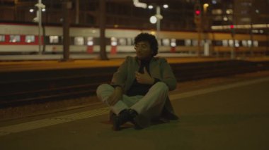 Siyah kıvırcık saçlı bir adam gece tren istasyonunda yalnız başına bekliyor. Yüksek kalite 4k görüntü