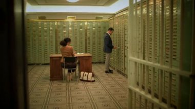 Profesyonel bir danışman müşteriye banka işlemleri için kasa dairesindeki kiralık kasalarını açmasında yardımcı olur.