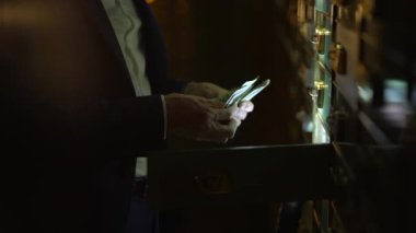 Loş, güvenli bir tesiste, bir adam mali güvence ortamında titizlikle para sayar.