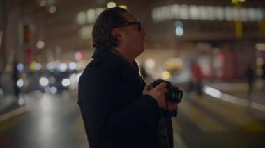 Bir fotoğrafçı gece kalabalık bir şehir caddesinde fotoğraf çekiyor. Şehir ışıklarını ve aktivitelerini yakalıyor..
