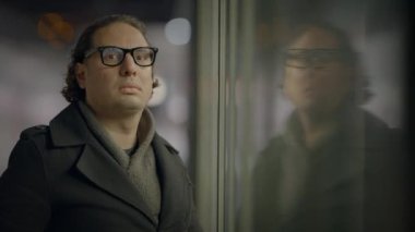 Gözlük takan profesyonel bir fotoğrafçı, cam bir pencerede yansımaları olan gece fotoğrafları çekiyor.