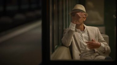 Bej takım elbiseli ve fötr şapkalı şık bir adam tren istasyonunda bekliyor. Pencereden yakalanmış..