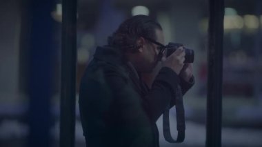 Bir erkek fotoğrafçı, gece şehir manzarası detaylarını özenle yakalıyor ve kameranın merceğine odaklanıyor.