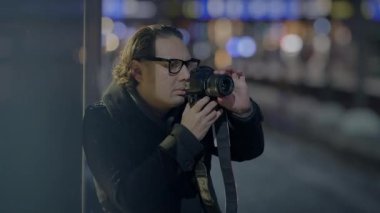 Şehir merkezinde bir fotoğrafçı, arka planda bulanık ışıklarla camlara yansıyan yansımaları yakalıyor..
