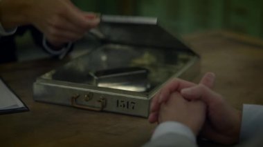 Bireylerin gizli belgelerini metal bir evrak çantası kullanarak değiş tokuş ettikleri bir iş toplantısının yakın çekimi..