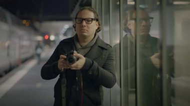 Elinde kamera olan bir adam gece tren istasyonunda görüntüler yakalıyor, cam duvara yansıyor..
