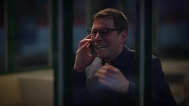 Parlak bir ofiste neşeli bir işadamı, neşeli bir şekilde gülüyor ve akıllı telefonuyla konuşuyor.