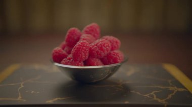 Mermer bir masada canlı ahududu dolu metal bir kase sergilenir, iştah açıcı ve taze bir sahne yaratır.