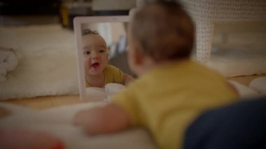 Canlı sarı tişörtlü şirin bir bebek, sıcak bir halının üzerinde midesinde kendi yansımalarıyla neşe içinde etkileşime girer.