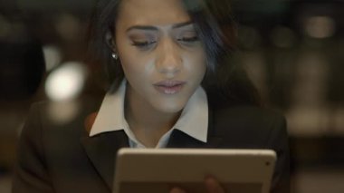 Kendini işine adamış bir iş kadını geç saatlere kadar çalışmak, profesyonellik ve kararlılık göstermek için ofisinde bir tablet kullanıyor.
