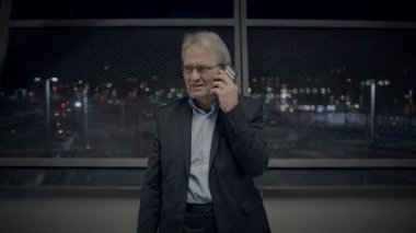 Üst düzey bir profesyonel gece geç saatlerde çağdaş bir ofis binasında telefonla konuşuyor.