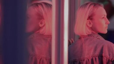 Parlak neon ışıklar ve modern ortamdaki yansımalar arasında duran kısa saçlı kişinin arka görünüşü.