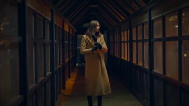 Uzun paltolu bir kadın gece aydınlık bir koridorda yalnız yürür, kasvetli bir ruh halinde yakalanır..