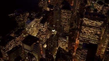 Parlak şehir gökdelenlerinin parlayan ışıklarıyla canlı şehir manzarasını gösteren, gece aydınlık gökdelenlerinin havadan çekilmiş fotoğrafı.