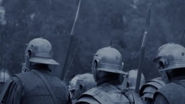 Miğferli ve zırhlı Romalı askerler tarihi bir yeniden canlandırma için hazırlanıyorlar, savaş düzeninde toplanıyorlar.