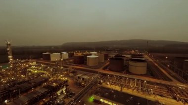 Hava kararırken endüstriyel petrol rafinerisinde büyük depolama tankları ve tesisleri gösteren panoramik bir çekim..