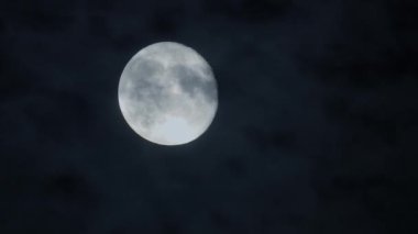Parlak dolunay bulutlu karanlık gece gökyüzünde parlıyor, dingin ve mistik bir atmosfer yaratıyor..