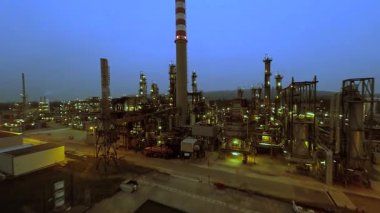 Büyük bir endüstriyel rafinerinin, makinelerin ve bacaların gece görüşü alacakaranlık altında aydınlandı.