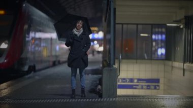 Yağmurlu bir şehirde yağmurlu bir akşamda yağmurlu bir tren platformunda sabırla duran şemsiyeli yalnız bir yolcu.