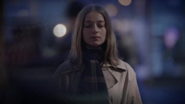 Kapalı gözlerle duran genç bir kadın, sakin bir anla sarmalanmış, kentsel bir gece sahnesinde huzuru buluyor.