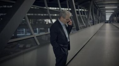 Bir işadamı, akşam saatlerinde modern bir yaya köprüsünde yürürken telefonla konuşuyor..