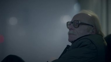 Gözlüklü yaşlı bir adam melankolik bir atmosfere sarılmış, gece tek başına otururken düşünür..