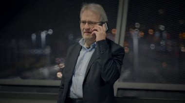 Bir iş adamı, şehirde gece vakti telefonuyla ciddi bir konuşma yapıyor.