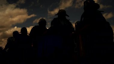Bir grup insan dramatik bir akşam gökyüzü altında birlik ve beraberlik hissi yaratmak için bir arada duruyorlar.
