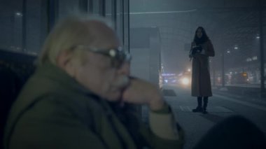 Şehirde sisli bir gecede bir kadın arka planda dururken yaşlı bir adam düşüncelere daldı..