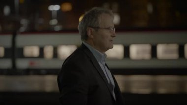 Profesyonel giyimli bir adam tren istasyonunda bekler, tren arka planda..