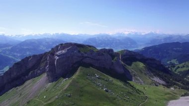 Berrak bir yaz gökyüzünün altında, vadilere ve uzak tepelere bakan nefes kesici bir dağ sırtı manzarası..