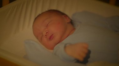 Sevimli, yeni doğmuş bir bebek beşikte huzur içinde uyuyor, rahat mavi pijamalar içinde, masumiyet ve sükunet yayıyor.