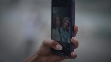 Yakın plan çekimde, arka planı bulanık iki arkadaşın resimlerini çeken bir akıllı telefon var..
