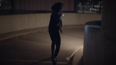 Elinde fener tutan bir kadının silueti, gece şehir ortamını keşfediyor. Gizemli ve ilgi çekici bir atmosfer..