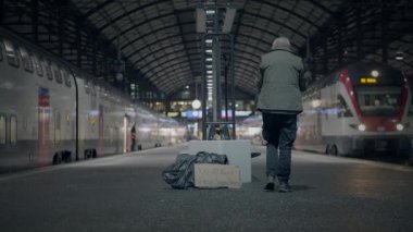 Geceleyin loş bir istasyonda iki tren arasında bir platformda duran yalnız bir yolcu..