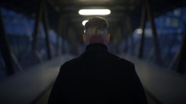 Boyun dövmesi olan biri karanlık bir tünelde tek başına yürürken görülüyor. Gizem ve yalnızlık hissi uyandırıyor.