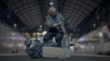 Tren istasyonunda bir bankta oturan bir adam, elinde yeşil bir klasör, yanında 