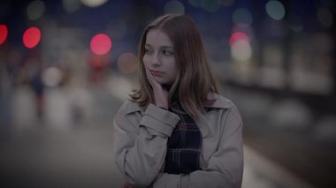 Bulanık şehir ışıklarıyla çevrili bir kış gecesinde şehir ortamında tefekkür eden genç bir kadın.