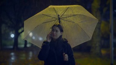 Yağmurlu bir gecede, şemsiyenin altında telefonla konuşan bir kadın görülüyor. Sahne kasvetli bir hava yayıyor..