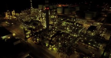 Aydınlatılmış yapılar, tanklar ve makinelerin sergilendiği büyük bir endüstriyel fabrikanın gece görüşü.
