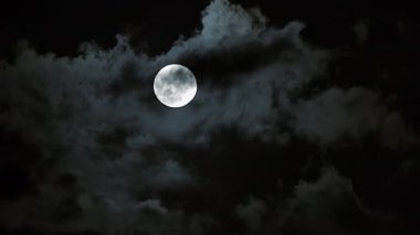 Dolunay, karanlık gece gökyüzünde dağılmış bulutların arasında parlıyor, dingin ve mistik bir atmosferi yakalıyor..